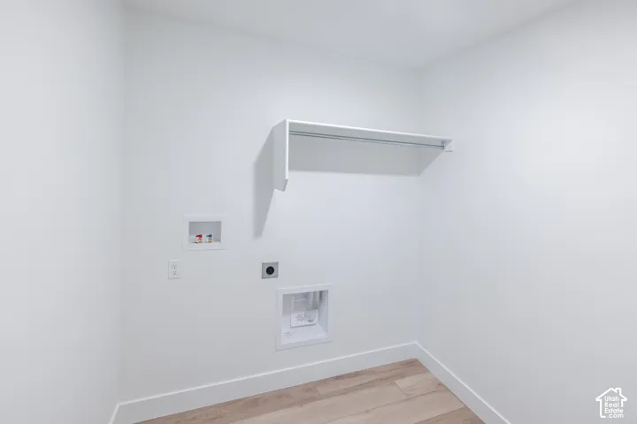 Utility space featuring wood-finish flooring, white walls, a built-in wall-mounted shelf with a rod, and recessed plumbing connections