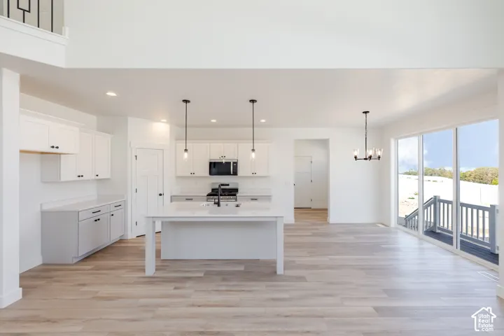 Open-concept kitchen featuring white cabinetry, a center island with a stone-surface countertop, recessed lighting, pendant fixtures, and wood-finish flooring