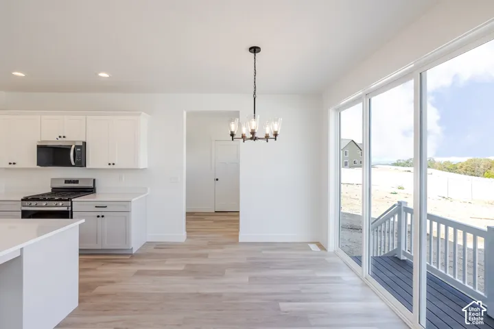 Kitchen featuring white shaker-style cabinetry, quartz countertops, a stainless steel over-the-range microwave, wood-finish flooring, and sliding glass doors with access to a deck