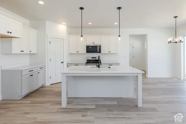 Kitchen featuring white shaker-style cabinetry, a central island with a solid surface countertop, wood-finish flooring, recessed lighting, and dual pendant light fixtures