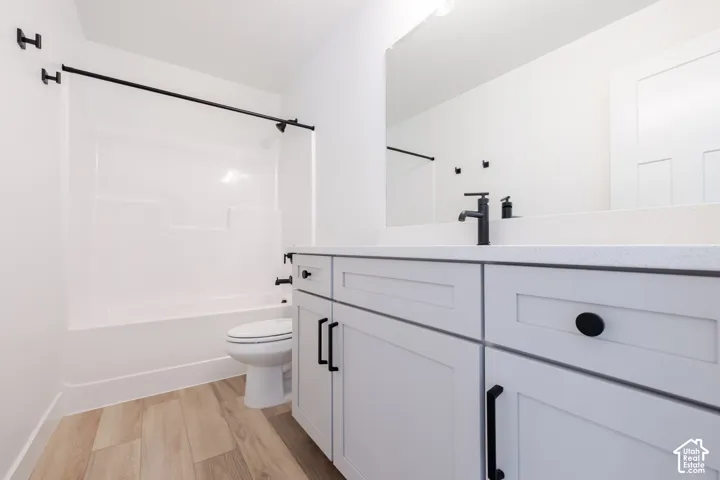 Bathroom featuring a white shaker-style vanity with stone-composite countertop, matte black hardware and fixtures, tub-shower combination, and wood-finish flooring