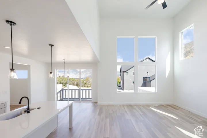 High-ceilinged living area featuring expansive floor-to-ceiling windows, wood-finish flooring, a kitchen island with stone-surface countertop, and matte black pendant lighting