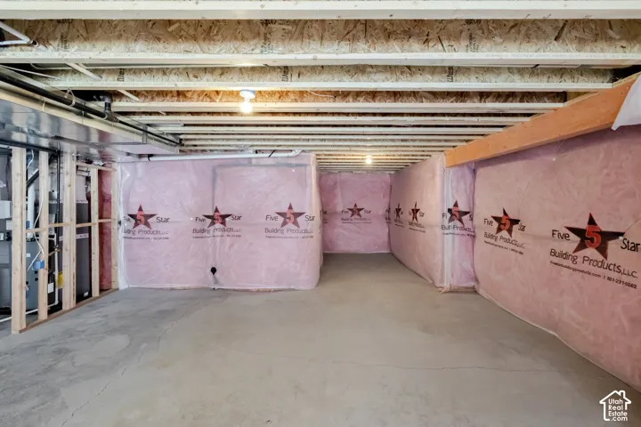 Unfinished lower level featuring concrete flooring, exposed wood joist ceiling, pink insulation wall wrap, and a metal furnace unit