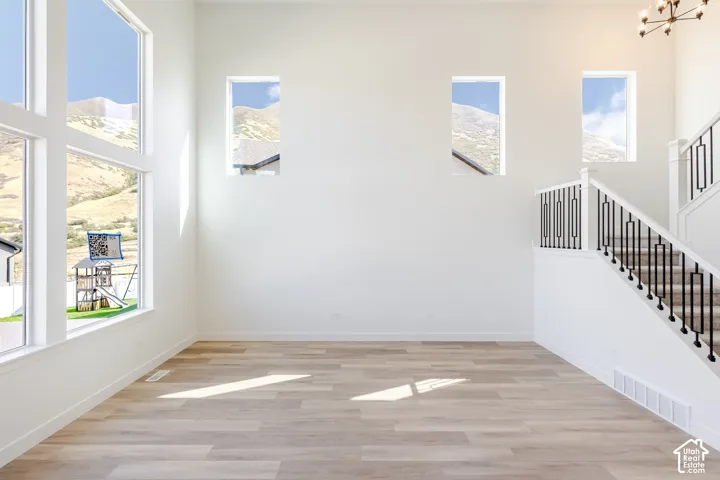 Double-height ceiling featuring oversized floor-to-ceiling windows, wood-finish flooring, mountain backdrop, and staircase with black metal balusters