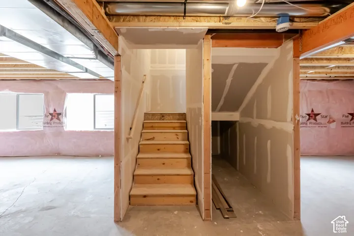 Unfinished interior area featuring exposed timber framing, concrete flooring, drywall-partitioned stairs, and dual egress windows
