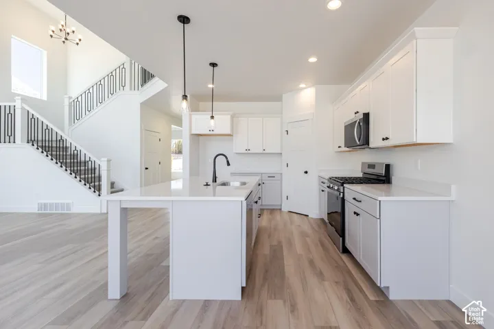 Kitchen featuring white cabinetry, quartz countertops, a central island with a matte black faucet, stainless steel appliances, and wood-finish flooring