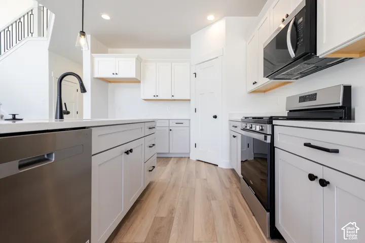 Kitchen featuring white shaker-style cabinetry, quartz countertops, stainless steel appliances, matte black hardware, and wood-finish flooring
