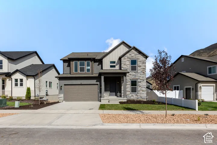 Two-story residence featuring a multi-material exterior of stone veneer and vertical siding, a covered front entryway, an attached two-car garage, and a manicured front lawn