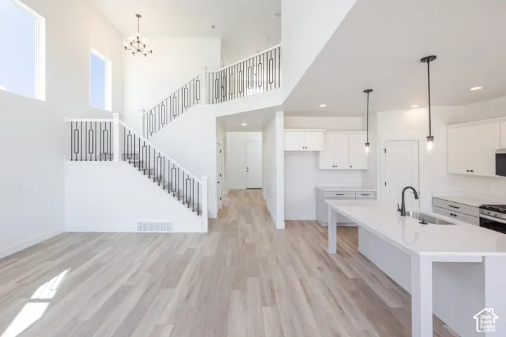 Open floor plan featuring wood-finish flooring, a kitchen island with stone-surface countertop, ceiling-height windows, a staircase with metal railings, and pendant lighting