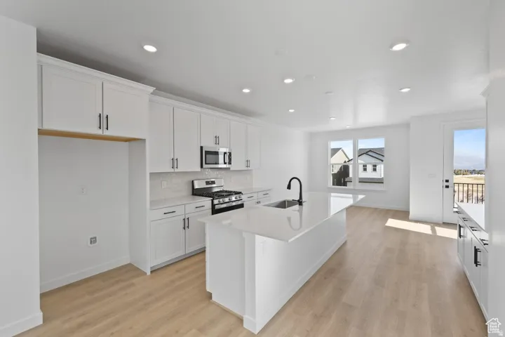 Contemporary kitchen featuring white cabinetry, a large center island with a sink, stainless steel appliances, and wood-finish flooring