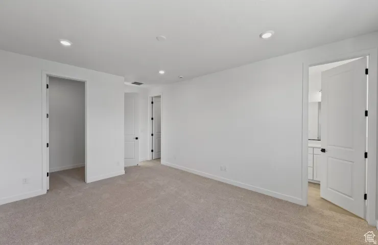 Spacious room featuring neutral carpet flooring, white walls, recessed ceiling lighting, and multiple panel doors with dark hardware