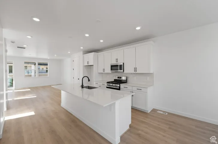 Contemporary kitchen featuring a large island with an undermount sink, white cabinetry with dark hardware, stainless steel appliances, and a tile backsplash
