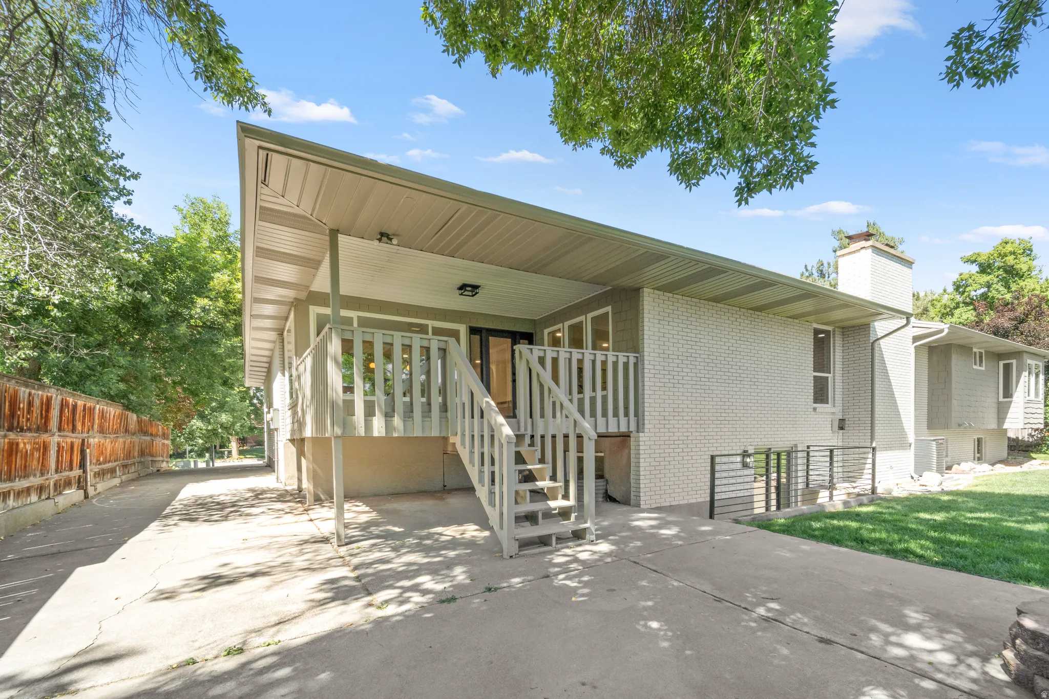 Rear exterior featuring a covered deck with railings, an extended concrete driveway, a chimney, and a lower-level access point with railings