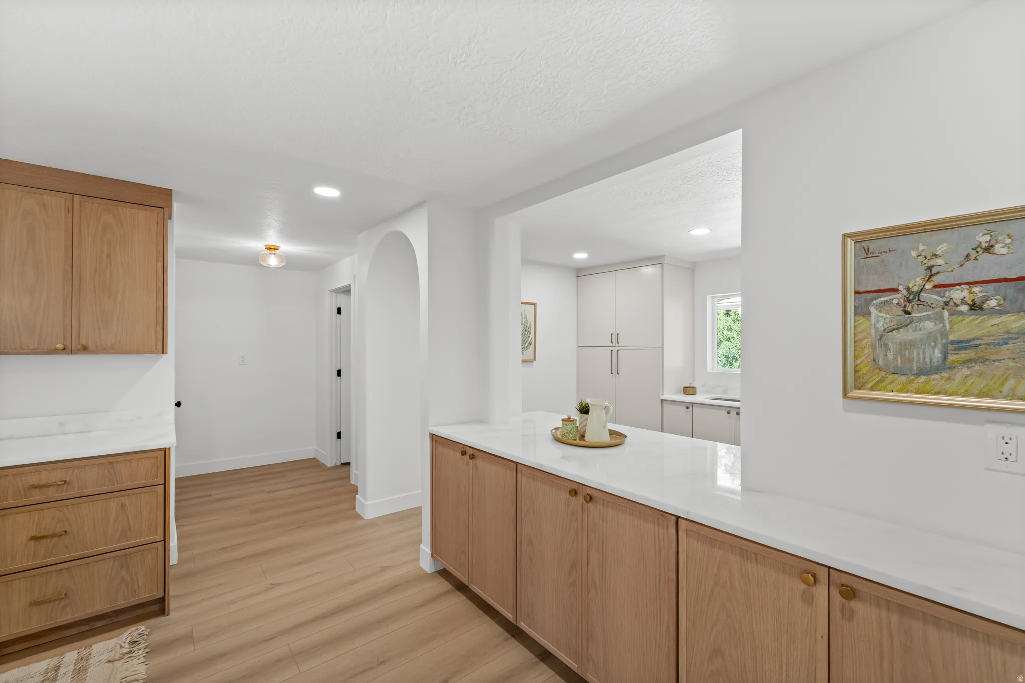Kitchen and hallway featuring wood-finish flooring and light wood cabinetry with brass hardware