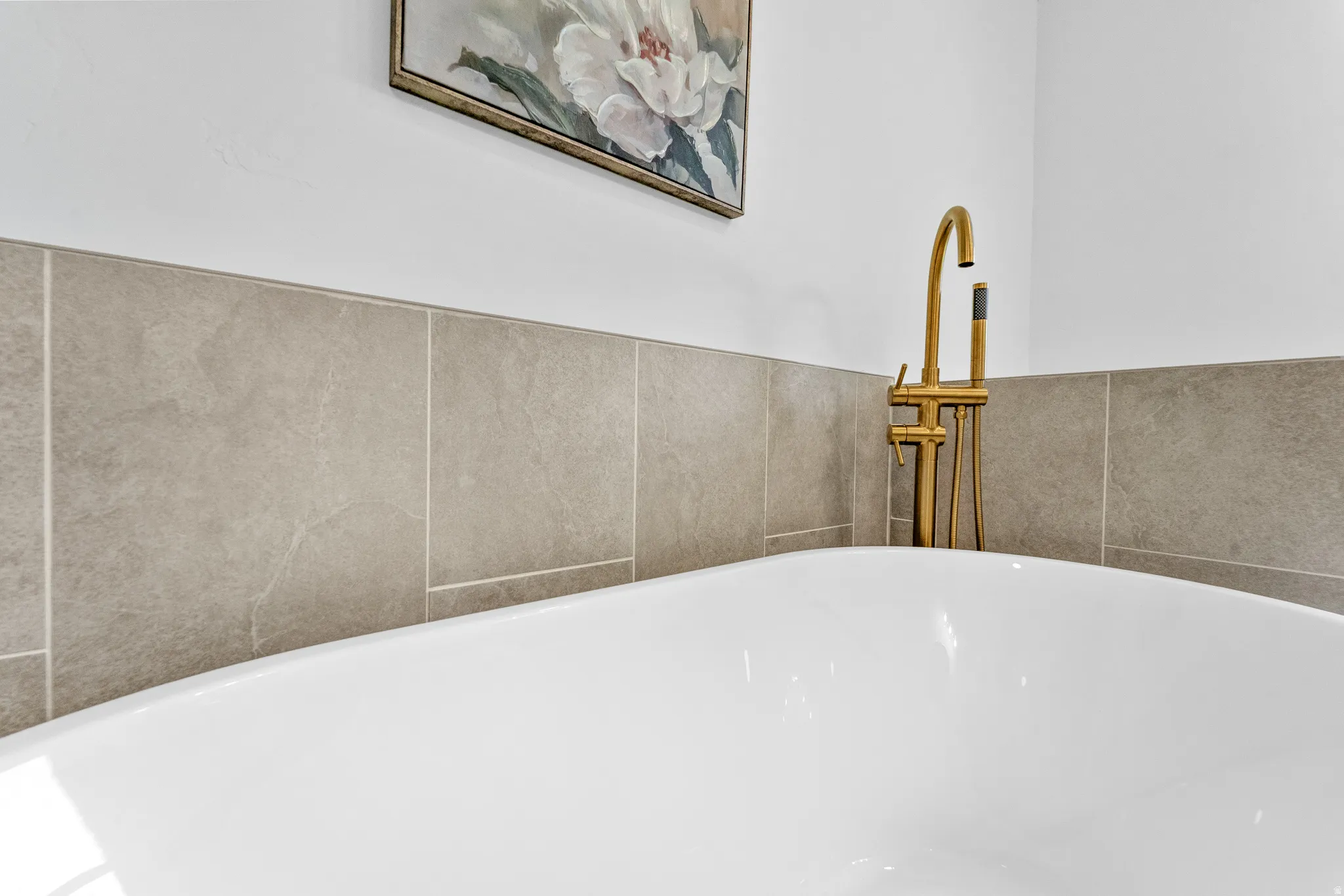 Freestanding soaking tub with a floor-mounted brass faucet, complemented by a tiled accent wall