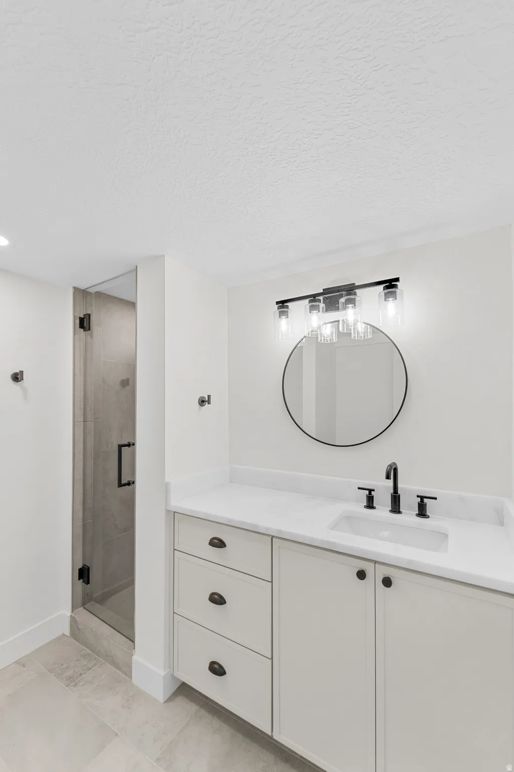 Bathroom featuring a white vanity with integrated sink, a circular mirror, and a four-light fixture