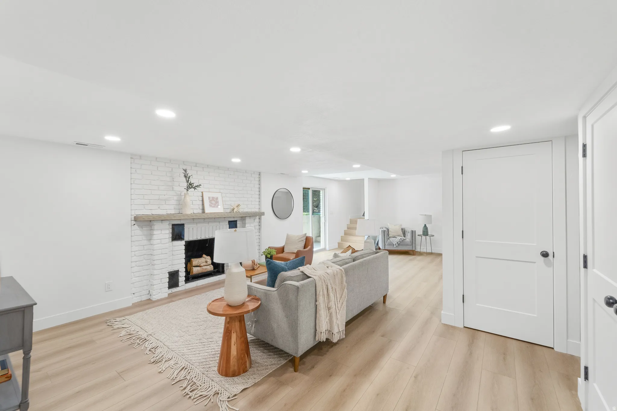 Spacious living area featuring a whitewashed brick fireplace with a wood mantel, wood-finish flooring, recessed lighting, and white paneled doors