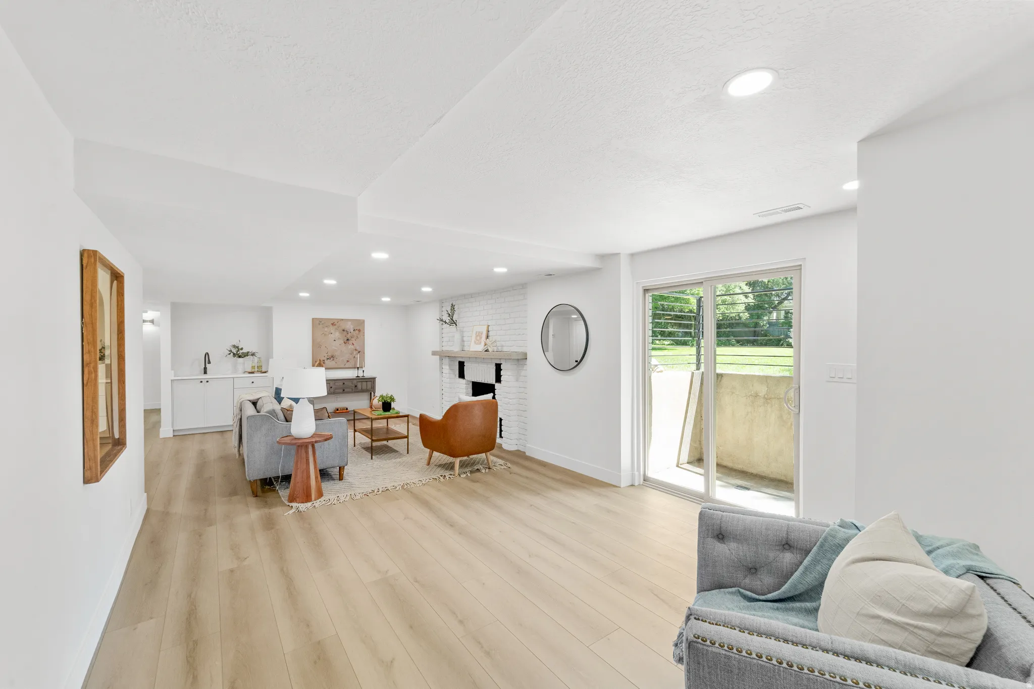 Spacious living area featuring light wood-finish flooring, recessed lighting, a white brick fireplace, and a built-in wet bar with white cabinetry