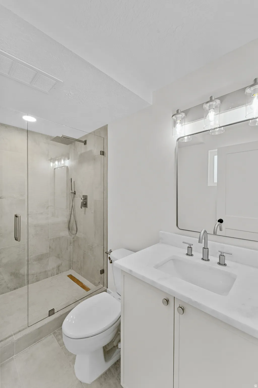 Bathroom featuring a glass-enclosed shower with a rainfall showerhead, a white vanity with a single basin sink, a wall-mounted mirror, and overhead vanity lighting