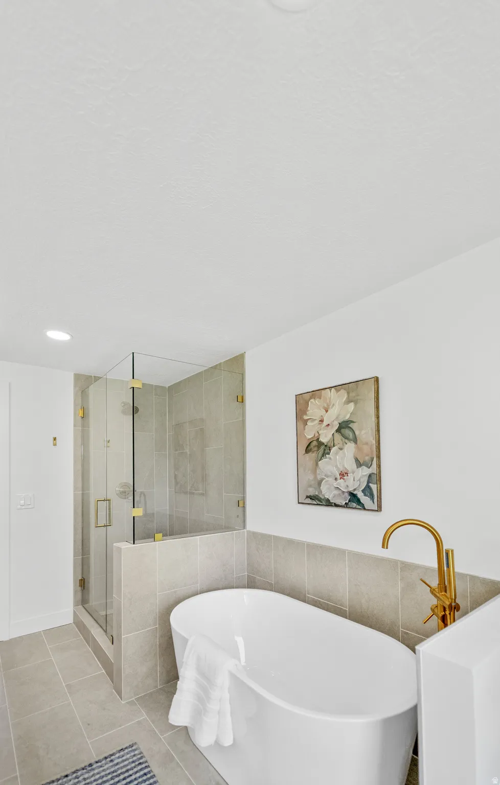 Freestanding soaking tub with a gold-finish floor-mounted faucet, complemented by a glass-enclosed shower with gold-finish hardware