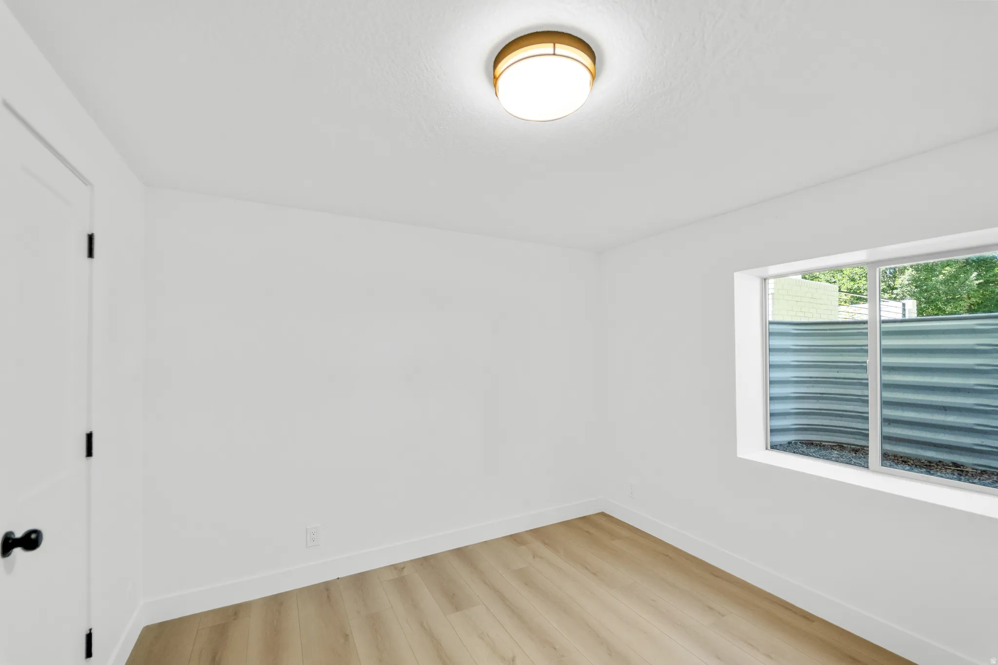 Bright interior room featuring wood-finish flooring, white walls, and a contemporary ceiling light fixture