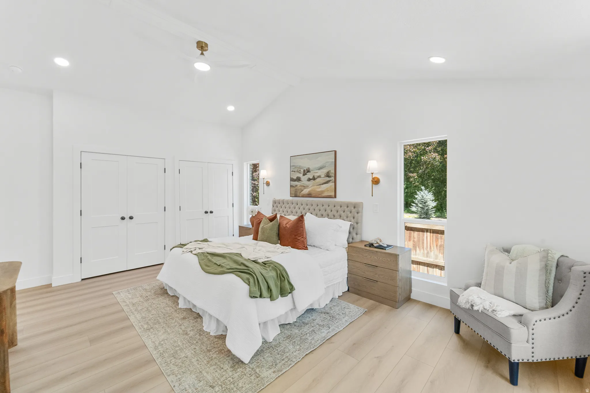 Vaulted ceiling bedroom featuring light wood-finish flooring, two sets of double-door closets, recessed lighting, and a ceiling fan