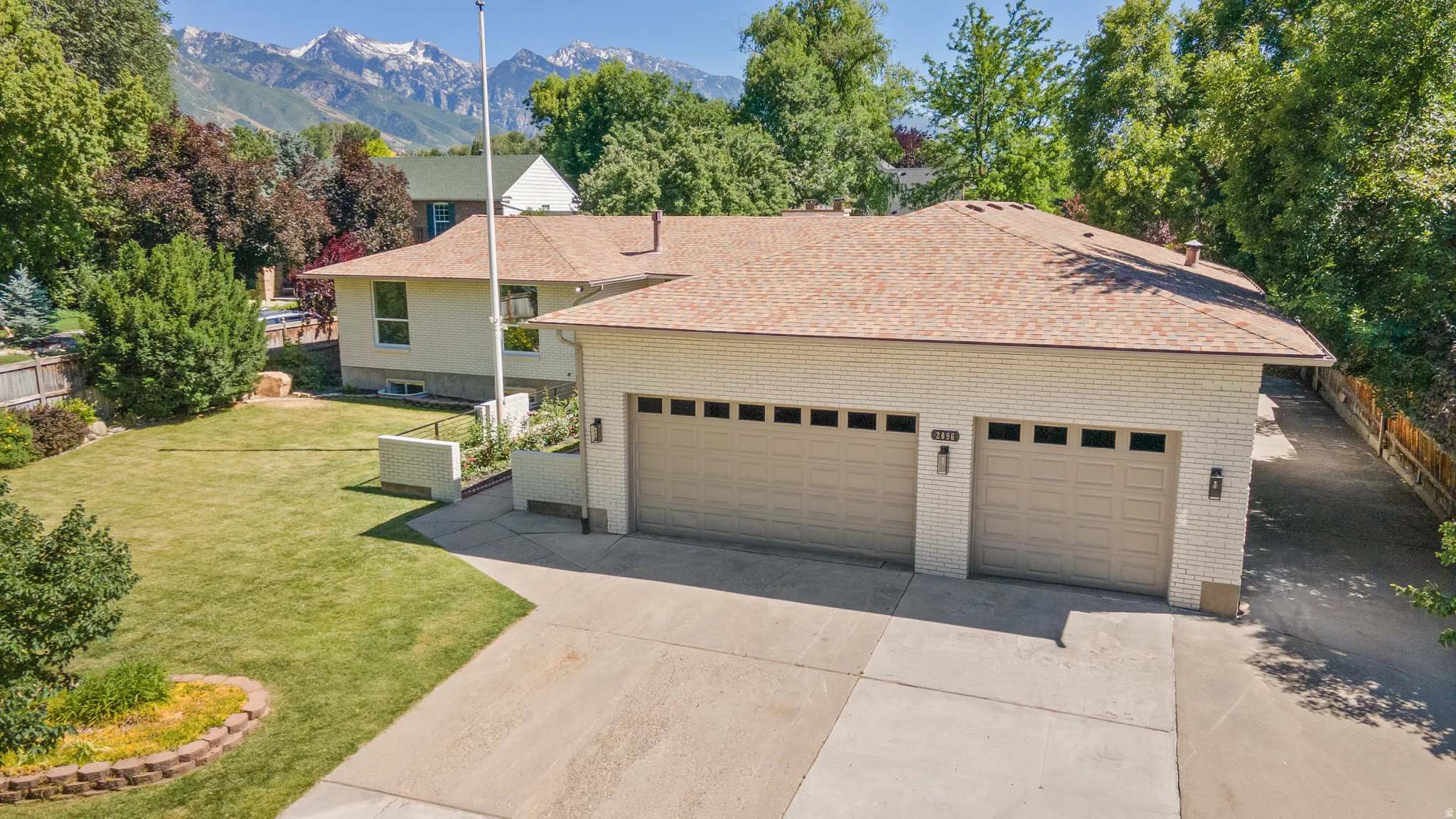 Light brick exterior with a multi-car garage, concrete driveway, and mature landscaping