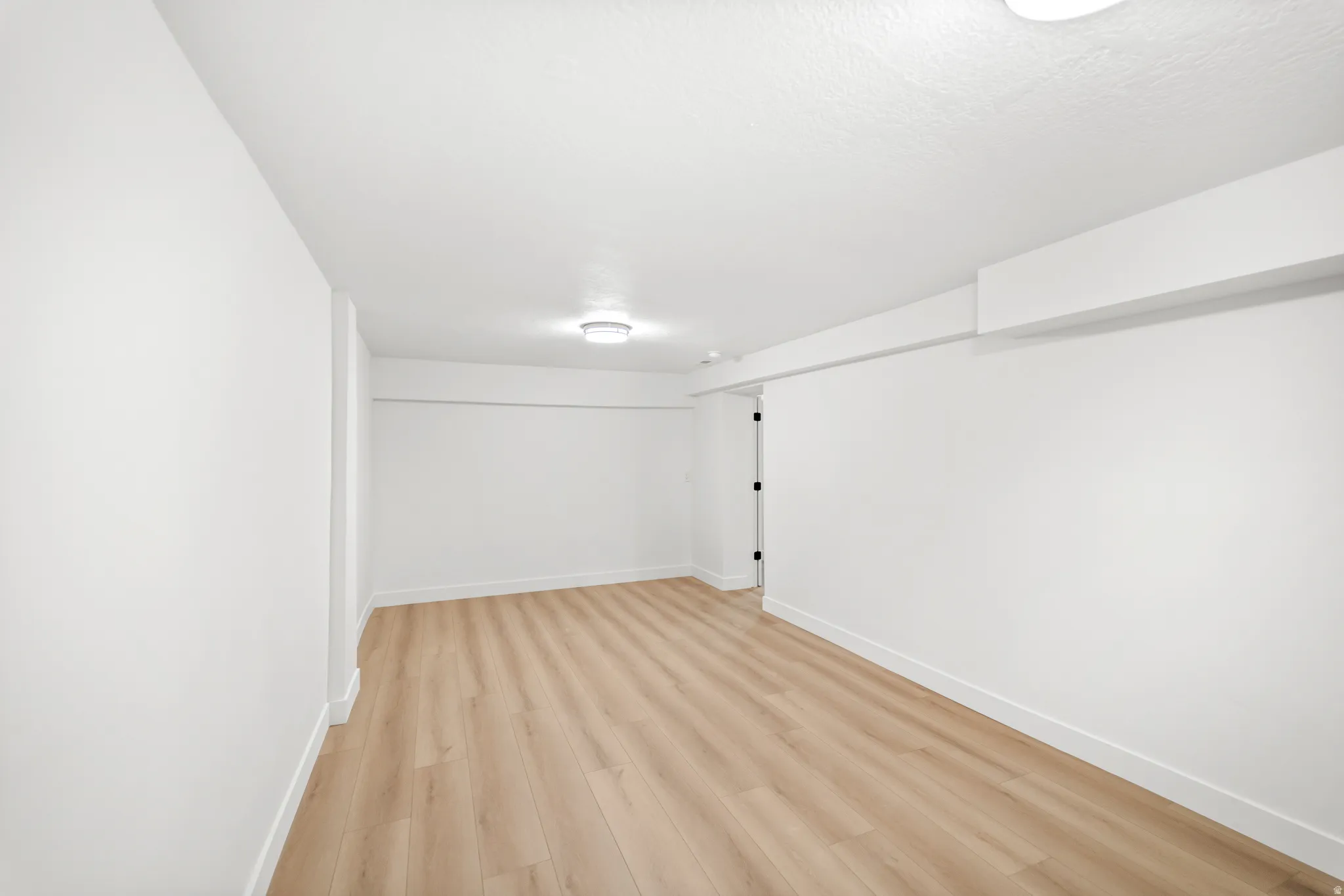 Spacious interior room featuring light wood-finish flooring, white walls, and bright overhead lighting