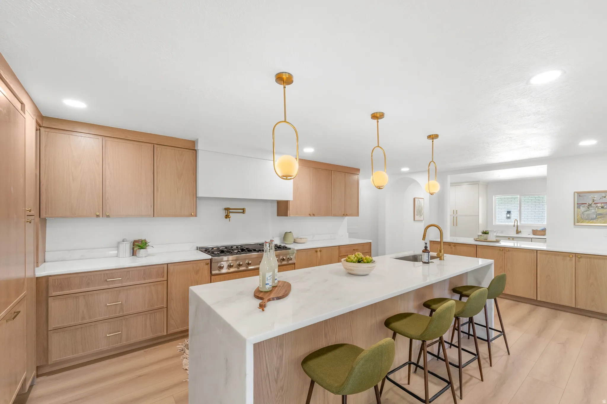 Gourmet kitchen featuring a large central island with seating, natural wood cabinetry, white stone countertops, and wood-finish flooring