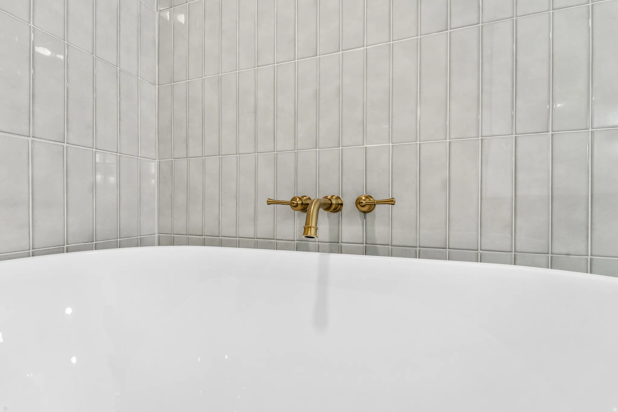 White soaking tub with wall-mounted brass fixtures and vertical subway tile surround
