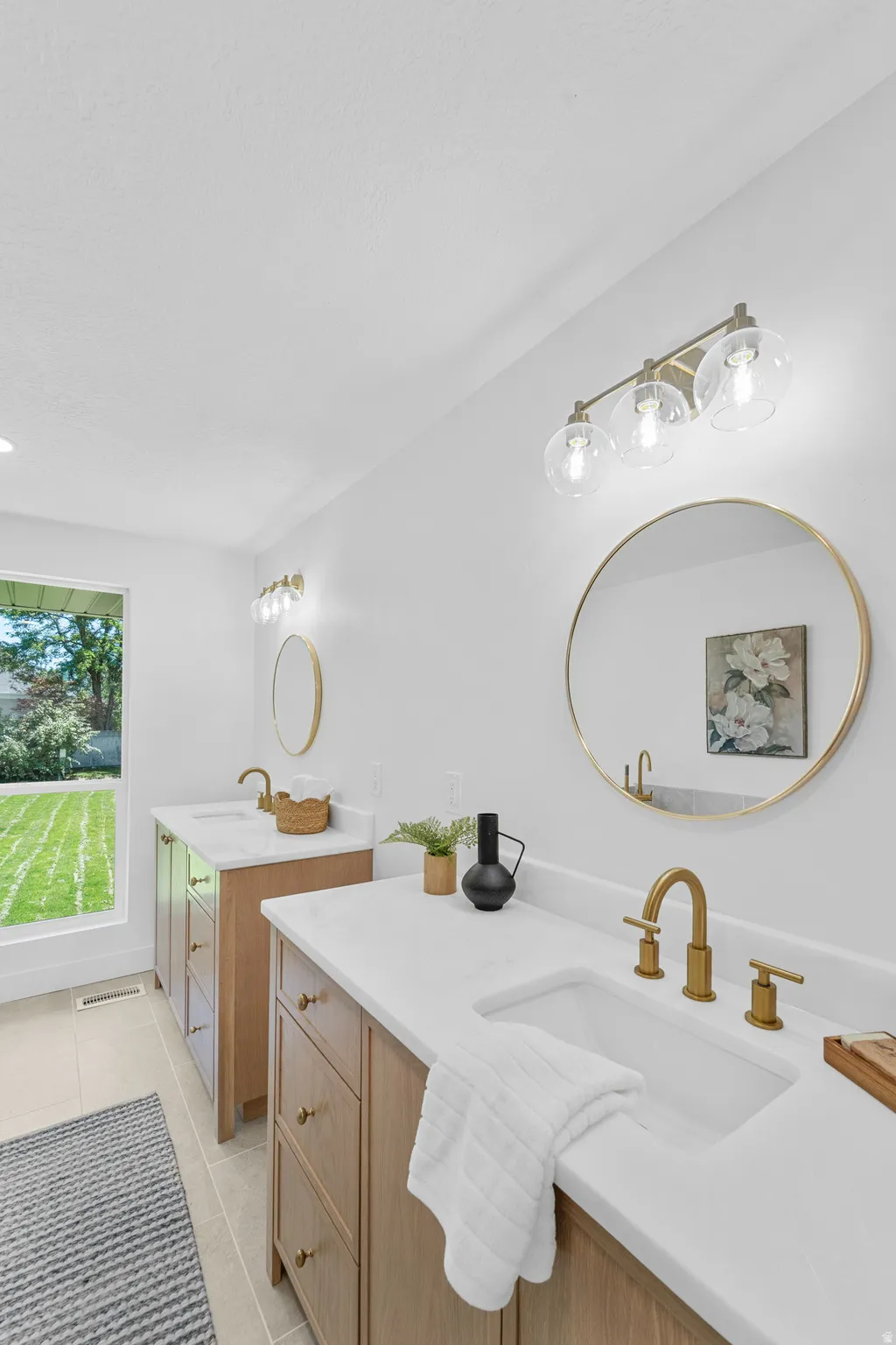 Dual vanity featuring light wood-finish cabinetry, white solid surface countertops, undermount sinks, and brushed gold fixtures