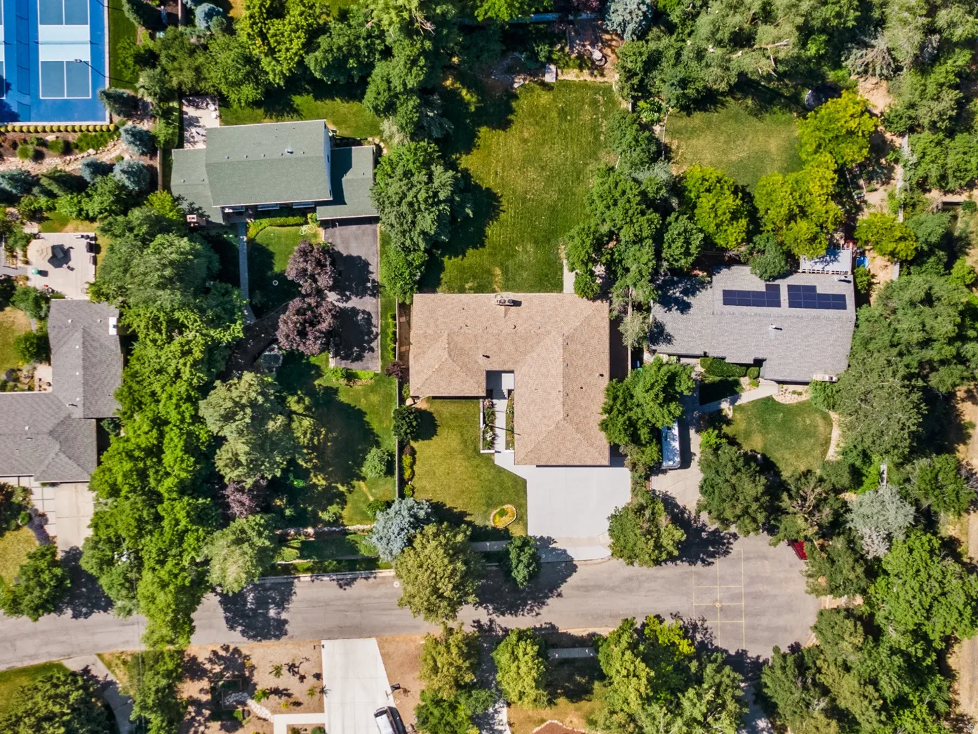 Aerial perspective showcasing a residential property with an L-shaped roofline, an expansive lawn, and a paved driveway
