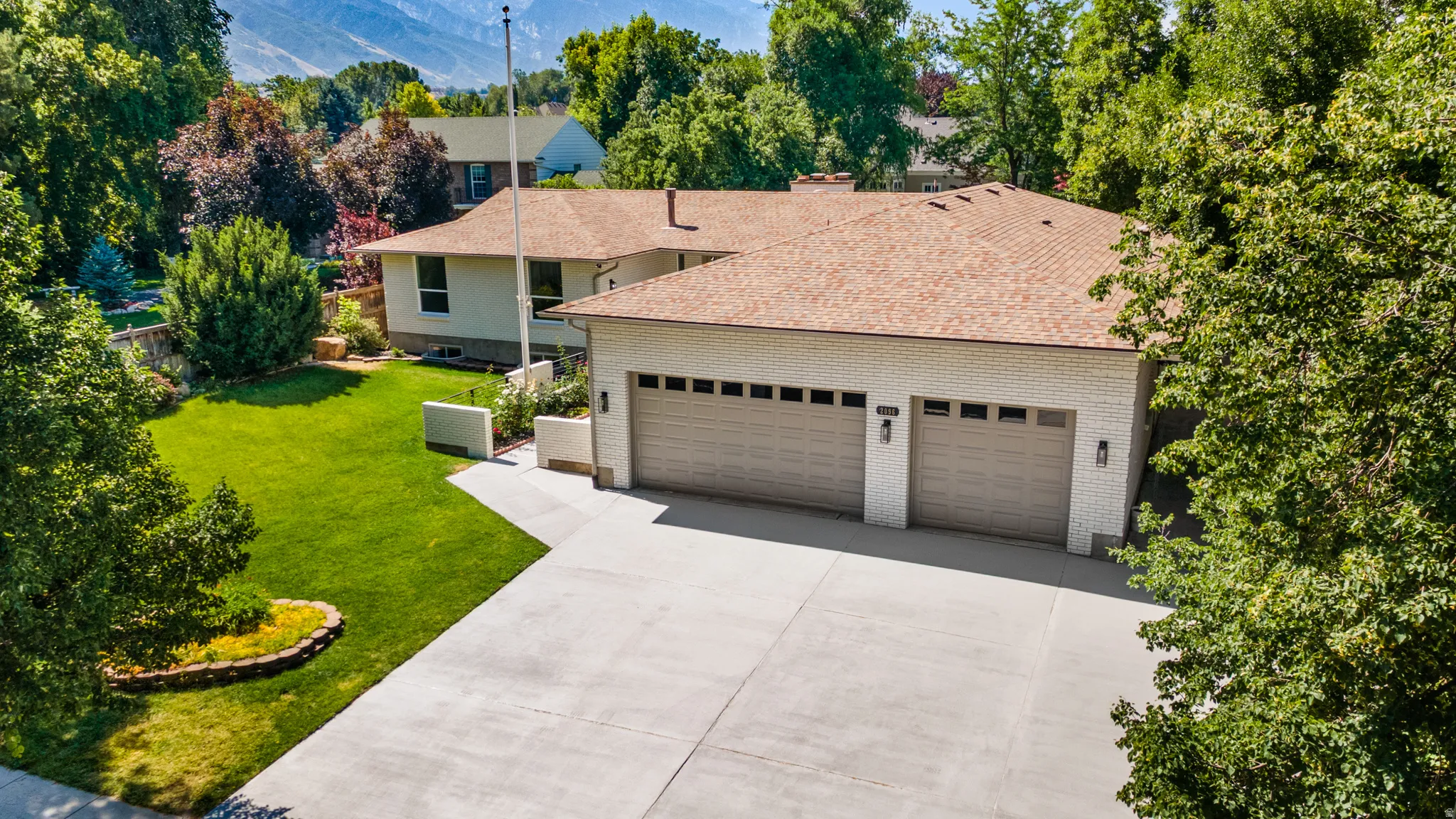 Expansive concrete driveway leading to a three-car garage with panel doors and exterior sconce lighting