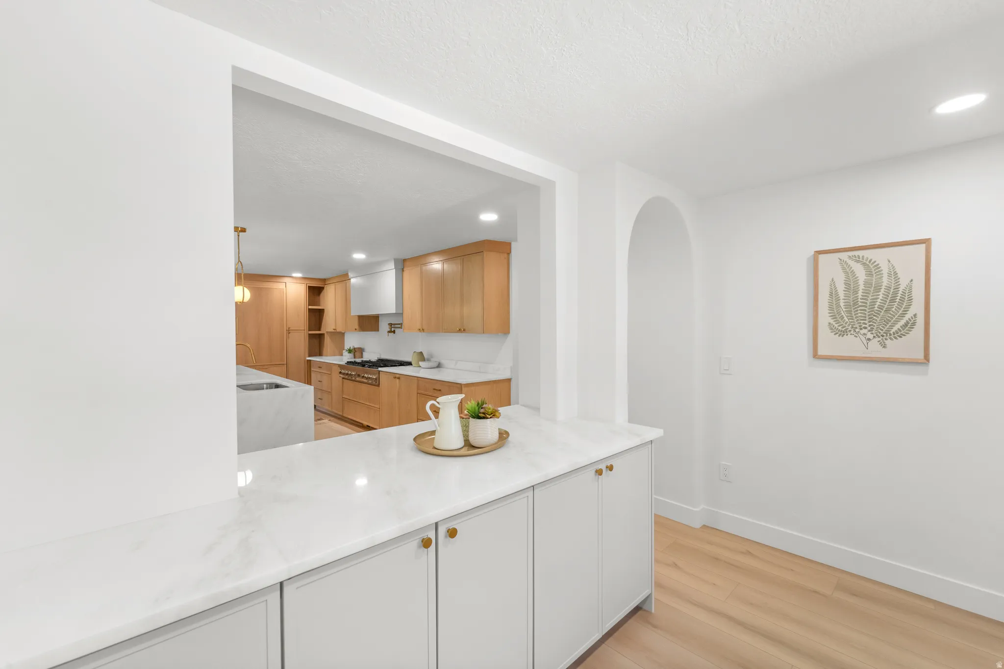 Kitchen featuring light wood-finish cabinetry, white stone countertops, and a full-height backsplash