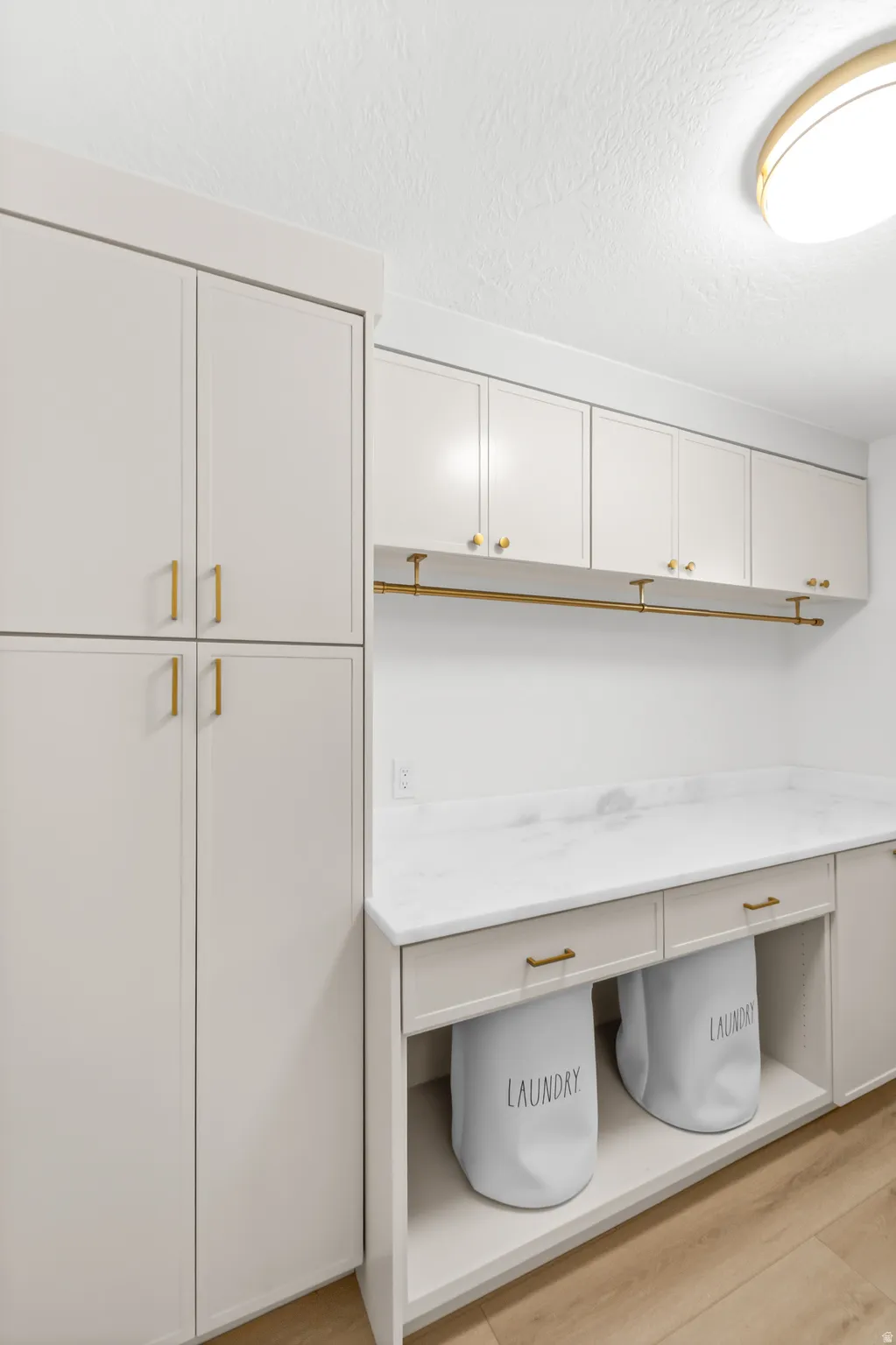Laundry area featuring extensive cabinetry, a marble-look countertop, brass-finish hardware, built-in storage solutions, and wood-finish flooring