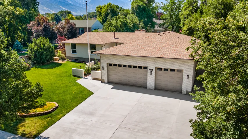 Expansive concrete driveway leading to a three-car garage with panel doors and exterior sconce lighting