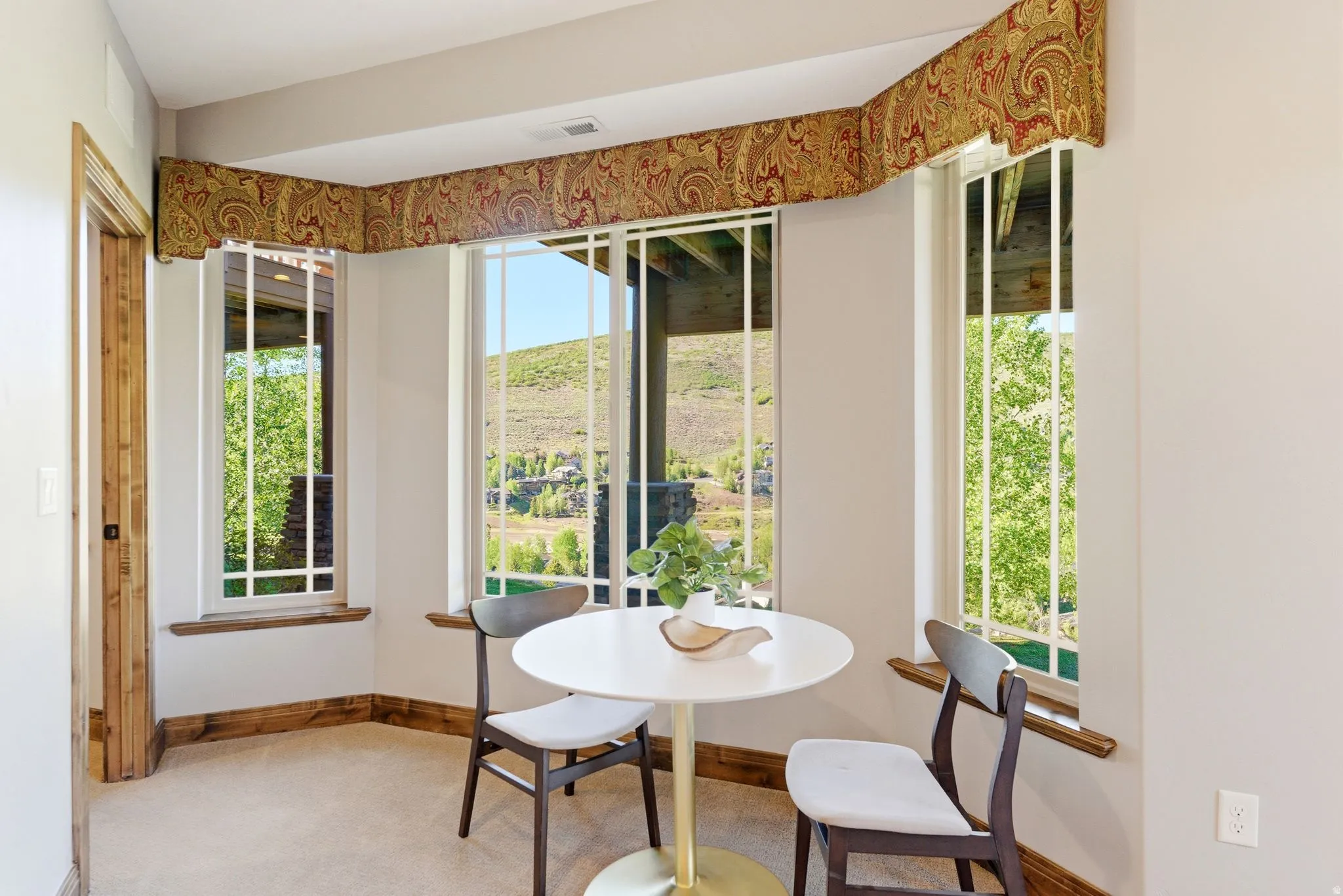 Bright corner alcove featuring multiple vertical windows with white mullions, a decorative fabric valance, and natural wood trim