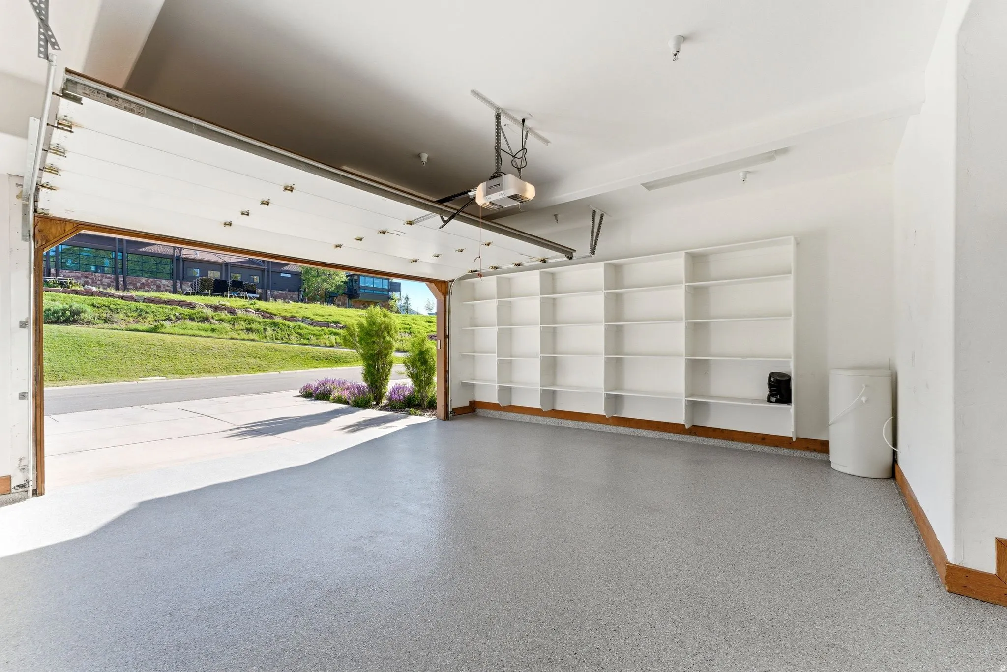 Spacious garage featuring an epoxy-coated floor, extensive built-in shelving, a transparent overhead garage door, and a permanent garage door opener