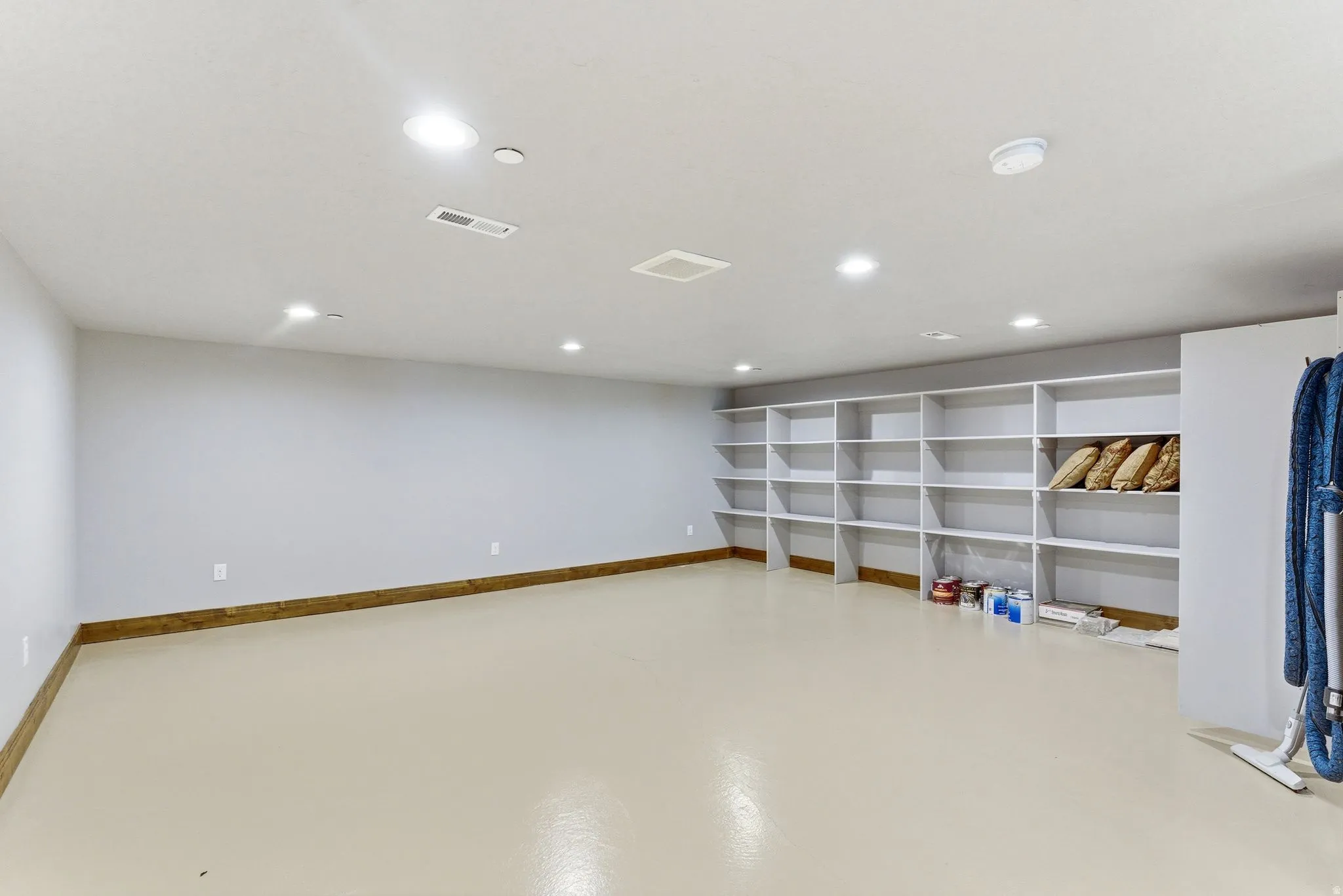 Spacious room featuring extensive built-in shelving, recessed ceiling lighting, light-toned flooring, and a contrasting wood-finish baseboard