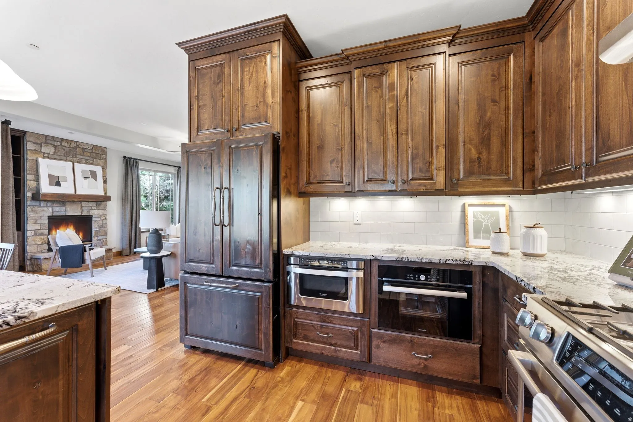 Gourmet kitchen featuring rich wood cabinetry, light-toned countertops, a white subway tile backsplash, stainless steel appliances, and wood-finish flooring
