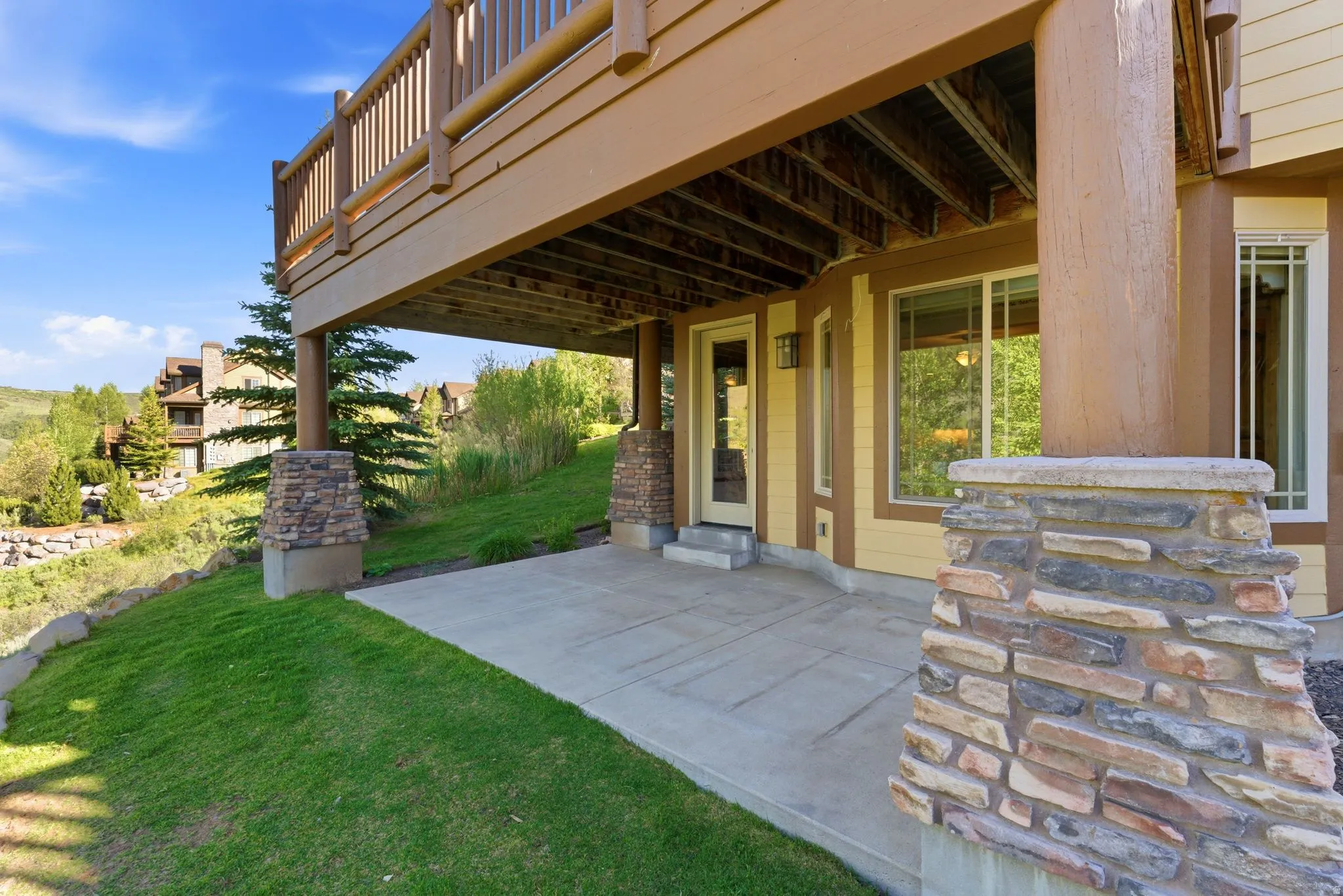 Ground-level patio with stone veneer columns supporting an upper-level wood deck