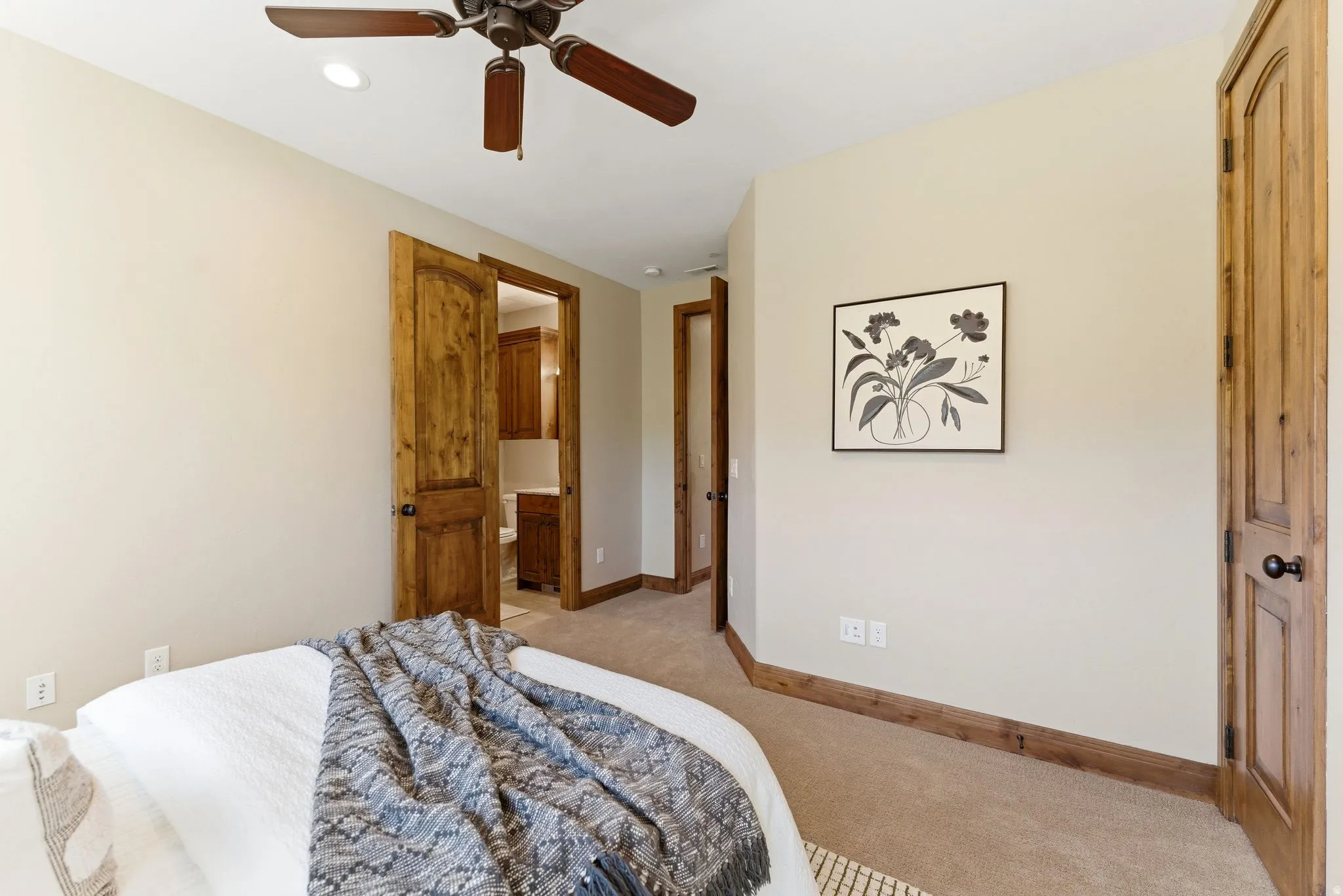 Carpeted room featuring a ceiling fan with integrated lighting, wood-finish doors with black hardware, and coordinating wood-finish baseboards