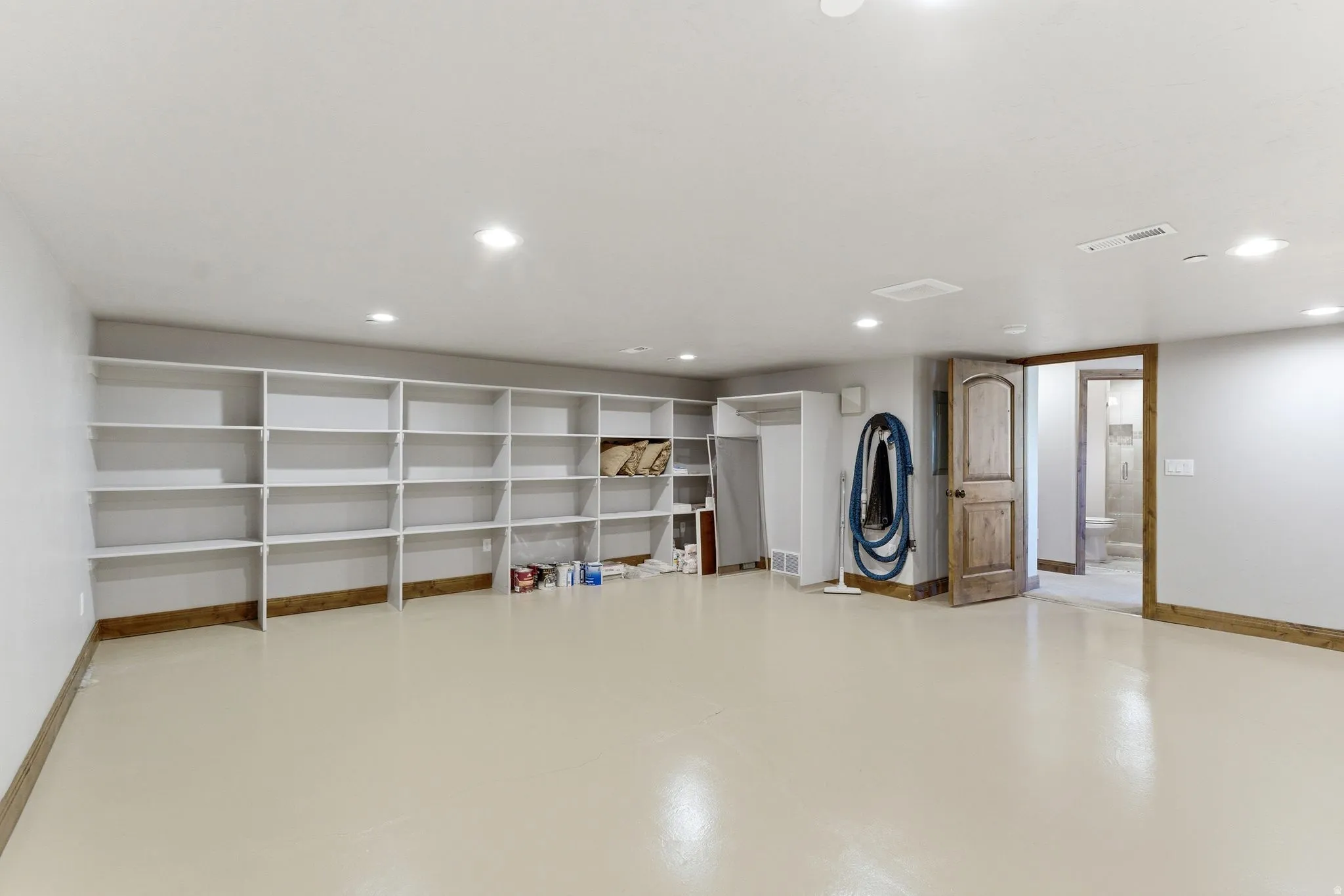 Expansive room featuring extensive built-in shelving, light-toned flooring, recessed lighting, and a wood-finish door with matching trim