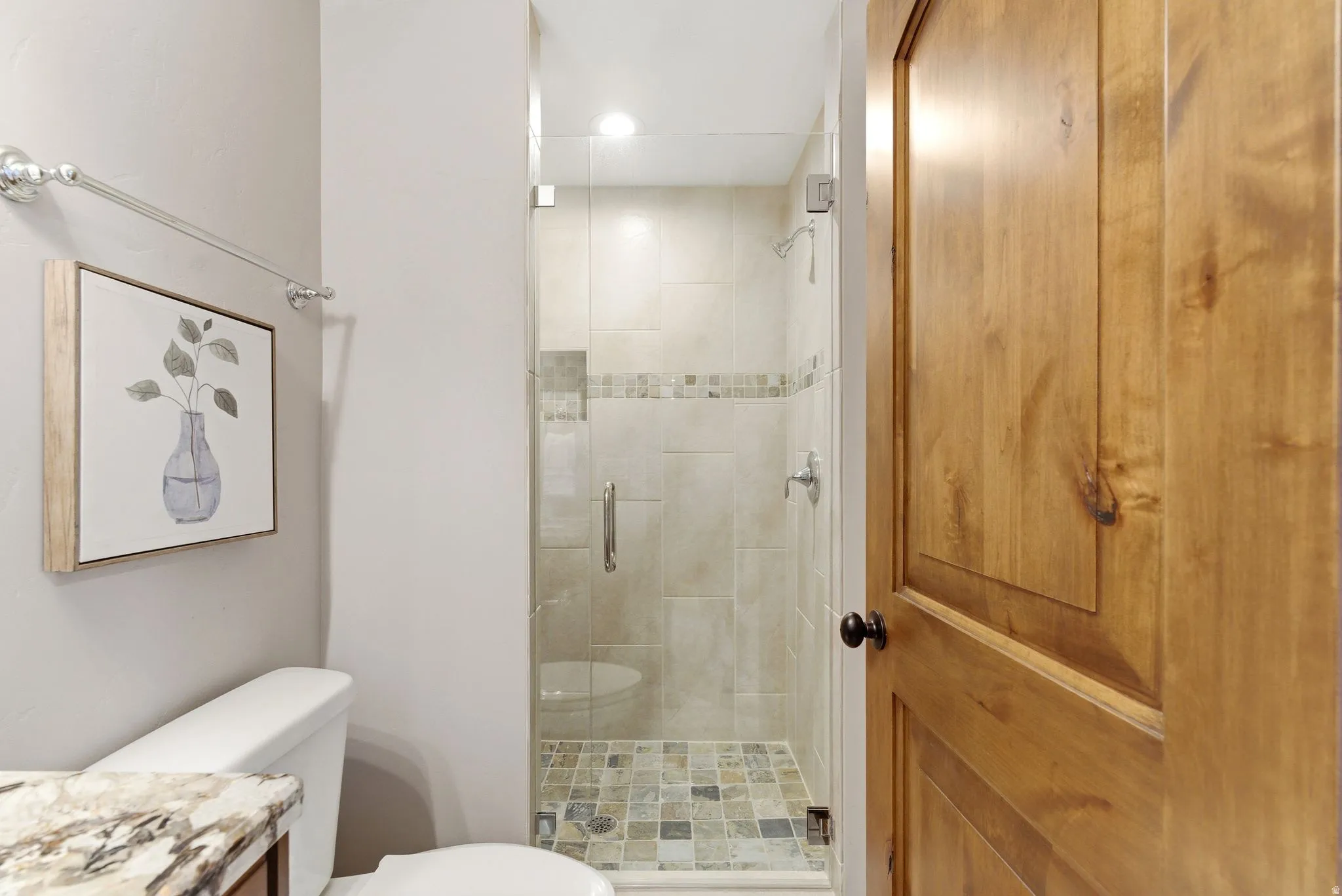Glass-enclosed shower featuring large format tile walls, a decorative mosaic tile band, and a mosaic tile floor