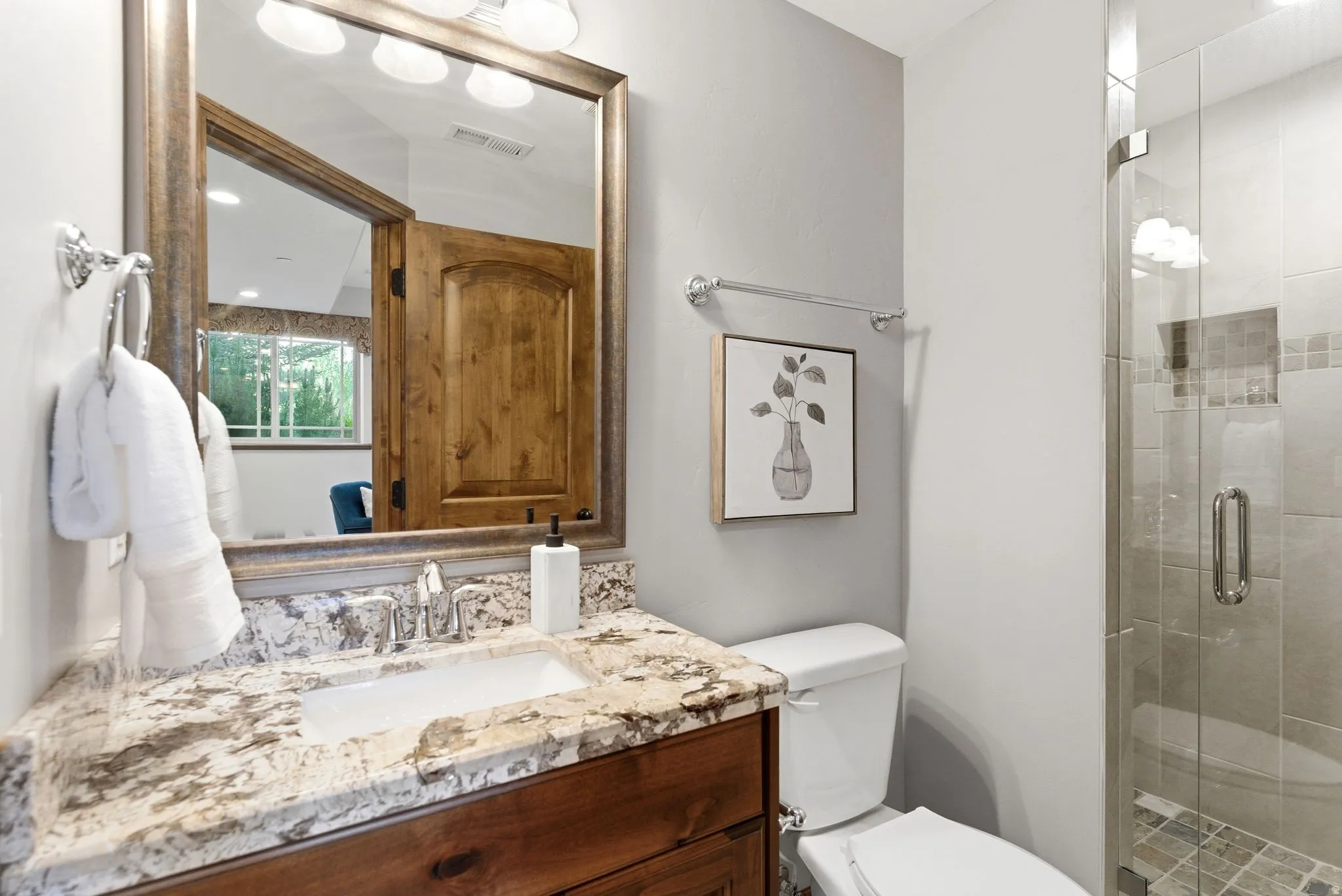 Bathroom featuring a wood-finish vanity with an undermount sink, a granite-style countertop, and a framed mirror with integrated lighting