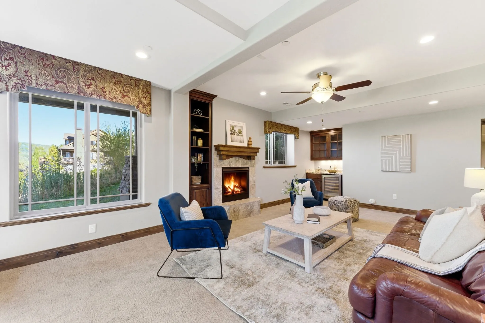 Living area featuring a stone fireplace with a wood mantle, built-in shelving, a wet bar with a beverage cooler, a ceiling fan, and recessed lighting