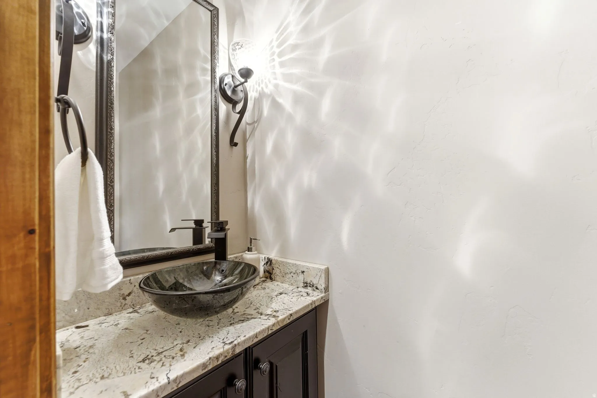 Vanity featuring a dark wood-finish cabinet with black hardware, a light-toned stone countertop, and a dark vessel sink