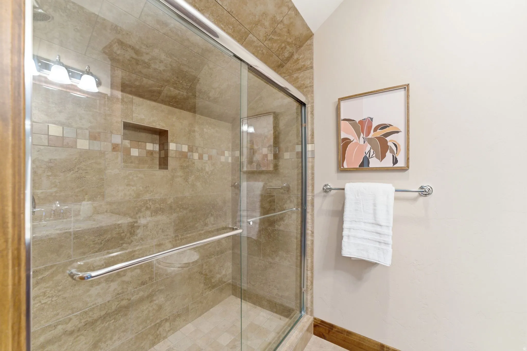 Glass-enclosed shower featuring natural stone-finish wall tile, a decorative mosaic tile band, and a built-in shower niche