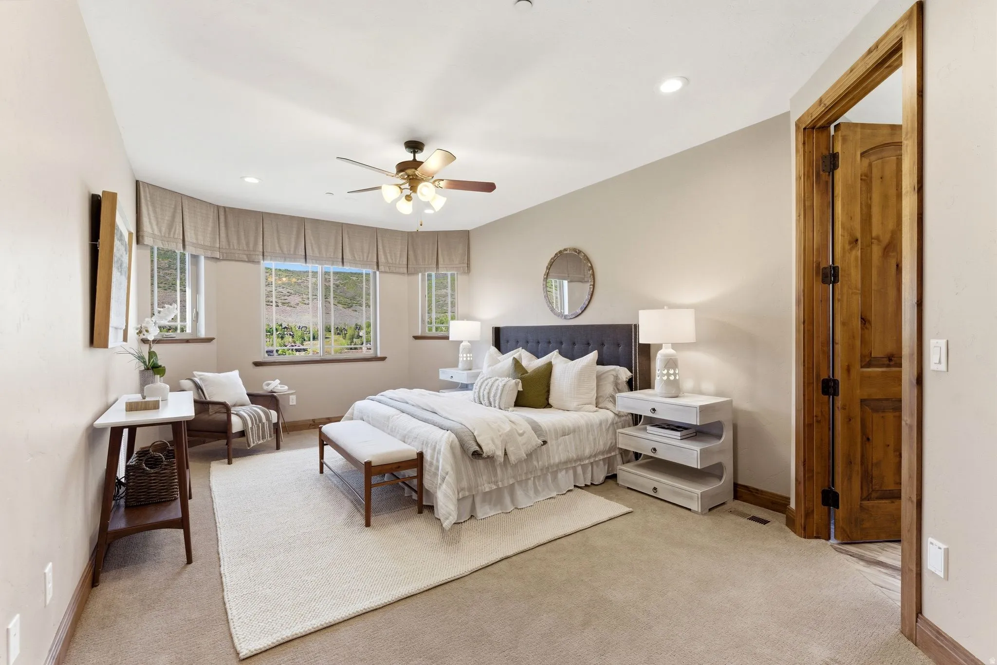 Carpeted bedroom featuring a large bay window, ceiling fan with integrated lighting, recessed lighting, a paneled wood door, and wood-finish trim
