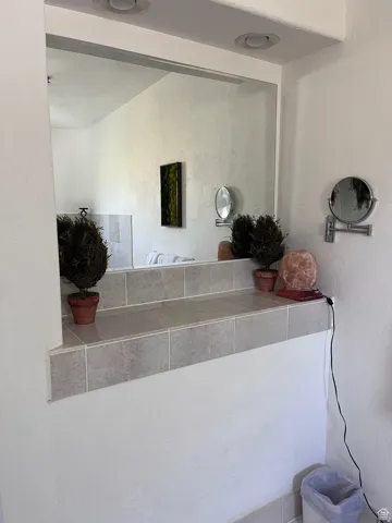 Recessed lighting illuminates a tile-framed pass-through opening with an integrated mirror
